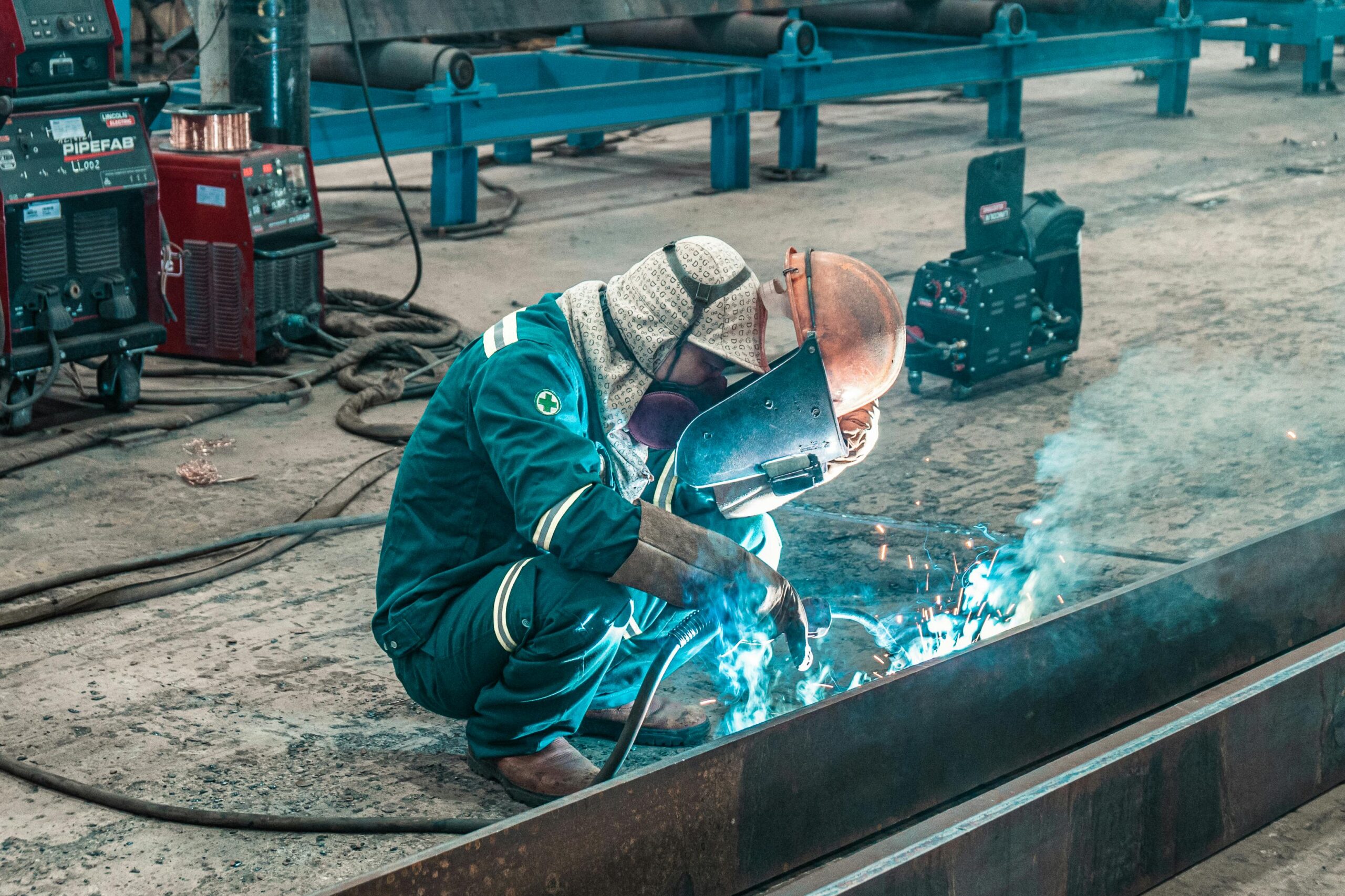 A welder using protective gear works on metal in a factory workshop.